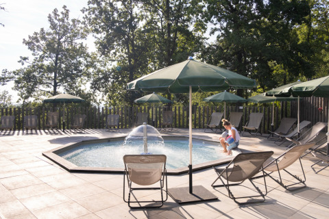 Piscina al aire libre con sombrillas verdes y tumbonas en Huttopia Wattwiller Glamping Grand Est.
