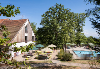 Huttopia Wattwiller - Glamping Grand Est met zwembad, buitenterras en groene bomen tijdens een zonnige dag.