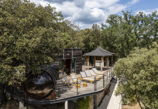 Terrasse ensoleillée avec transats, chalet en bois et spa entouré d’arbres au Domaine de Sévenier & Spa.