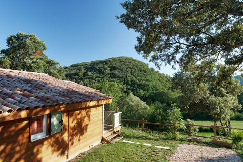 Cabaña de madera en Domaine de Sévenier & Spa, rodeada de colinas y vegetación en Auvergne-Rhône-Alpes.