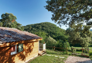 Wooden chalet with tiled roof at Domaine de Sévenier & Spa, surrounded by hills and greenery in Auvergne-Rhône-Alpes.