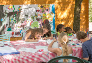 Kinderen knutselen aan een buitentafel bij Domaine de Sévenier & Spa glamping, Auvergne-Rhône-Alpes.