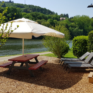 Glamping-Unterkunft Camping Fortuna am Neckar mit Picknicktisch, Sonnenliegen und Zigeunerwagen am Flussufer.