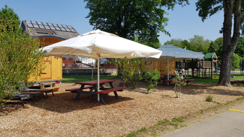 Zona de glamping con mesas de picnic, sombrillas y caravana de madera en Camping Fortuna am Neckar.