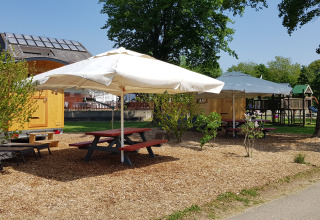 Zona de glamping con mesas de picnic, sombrillas y caravana de madera en Camping Fortuna am Neckar.