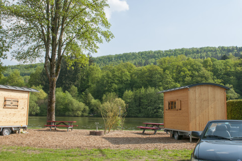 Glamping al Camping Fortuna am Neckar con roulotte in legno, tavoli da picnic e auto vicino al fiume.