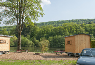 Glamping en Camping Fortuna am Neckar con cabañas de madera, mesas de picnic y coche junto al río.