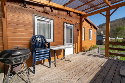 Veranda in legno con barbecue, sedie di plastica e tavolo davanti al bungalow glamping di Camping Hetzingen - Stacaravans Nordrhein-Westfalen.