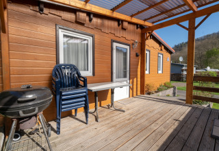 Terrasse en bois avec barbecue, chaises en plastique et table devant le bungalow à Camping Hetzingen - Stacaravans Nordrhein-Westfalen.