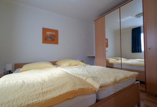 Camera da letto luminosa con letto matrimoniale, biancheria gialla, quadro e armadio con ante a specchio.