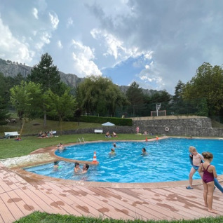 Børn og voksne nyder udendørs pool på Huttopia Barcelona Pirineos Glamping, omgivet af bjerge og skov.