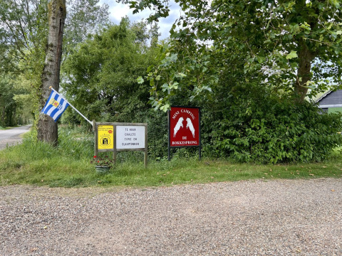 Eingang zum Mini Camping De Bokkesprong mit Flagge, Schildern und Natur, Glamping und Chalets verfügbar.