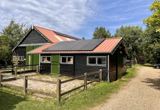 Edificio negro de madera con paneles solares en el techo en Glamping De Bokkesprong, rodeado de árboles.