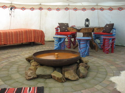 Interno di una tenda di lusso a Glamping - De Bokkesprong, con focolare, letto e area salotto colorata.