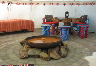 Interior de tienda de lujo en Glamping - De Bokkesprong, con chimenea, cama y área de asientos colorida.