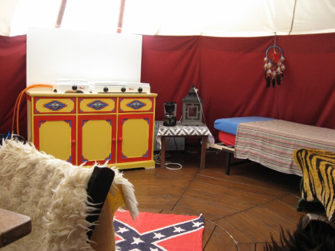 Interieur van een glamping-tent met gekleurd kastje, bed, koffiezetapparaat en confederatie-vloerkleed.