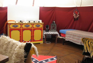 Interior of glamping tent with colorful cabinet, bed, coffee maker and confederate flag rug on wooden floor.