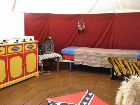 Vista interna dell'alloggio glamping De Bokkesprong con cucina colorata, letto e decorazioni caratteristiche.