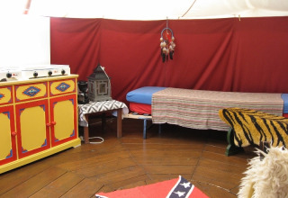 Vue intérieure d’un hébergement glamping chez De Bokkesprong, avec cuisine colorée, lit et décorations.