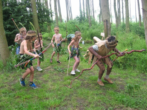 Children and an adult dressed as cavemen play in the forest at the Glamping - De Bokkesprong campsite.