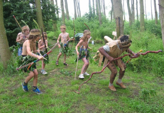 Kinder und ein Erwachsener als Steinzeitmenschen verkleidet spielen im Wald bei Glamping - De Bokkesprong.