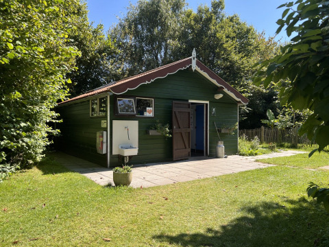 Groen glampinghuisje met rood dak en open deur in groene tuin bij Glamping - De Bokkesprong in Nederland.