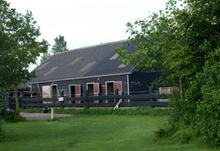 Hébergement glamping De Bokkesprong aux Pays-Bas, grange noire entourée d’arbres et pelouse verte