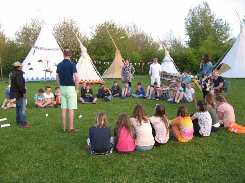 Kinder und Erwachsene sitzen im Kreis vor Tipis bei Glamping - De Bokkesprong und genießen das Beisammensein.