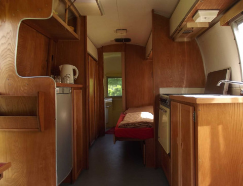 Vista interior de una caravana Airstream vintage con muebles de madera, cocina y cama en hotel glamping.