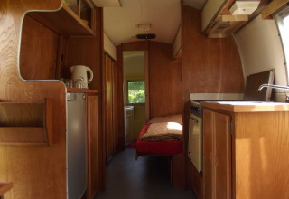 Innenansicht eines Vintage Airstream Wohnwagens mit Holzdekor, Bett und Küche im Glampingstil.