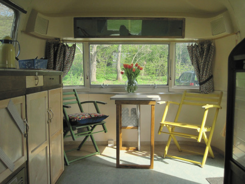 Indretning af en vintage campingvogn med sollys, to stole, et lille bord og blomster i glasvase i Airstream Hotel.