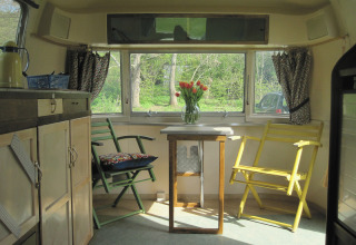 Gezellig interieur van een vintage caravan met tafel, twee stoelen en bloemenvaas in Airstream Hotel - Vintage Caravan.