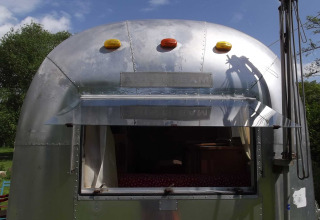 Vooraanzicht van een vintage Airstream-caravan als glamping accommodatie met open raam in Thüringen.