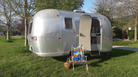 Glamping in een vintage Airstream caravan met open deur, kleurrijke stoel en mand in groen Thüringen.