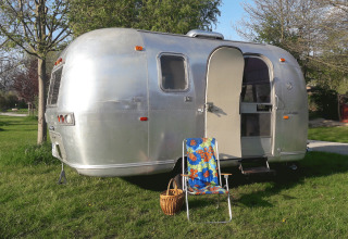 Glamping en una caravana Airstream vintage con puerta abierta, silla colorida y cesta en césped verde en Turingia.