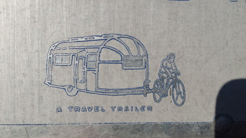 Zeichnung eines Vintage-Wohnwagens, der von einem Radfahrer gezogen wird, mit der Aufschrift 'A TRAVEL TRAILER', inspiriert vom Airstream Hotel.