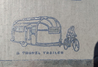 Zeichnung eines Vintage-Wohnwagens, der von einem Radfahrer gezogen wird, mit der Aufschrift 'A TRAVEL TRAILER', inspiriert vom Airstream Hotel.