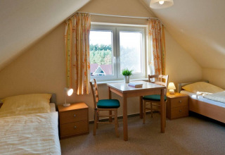 Chambre lumineuse avec deux lits simples, mobilier en bois et vue par la fenêtre à Havelberge.