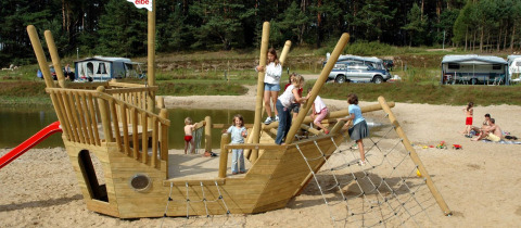 Children play on a wooden pirate ship playground at the beach at Vakantiepark Havelberge glamping site.