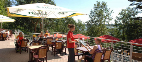 Udendørs terrasse på Vakantiepark Havelberge feriepark i Mecklenburg-Vorpommern med gæster og serveringspersonale.