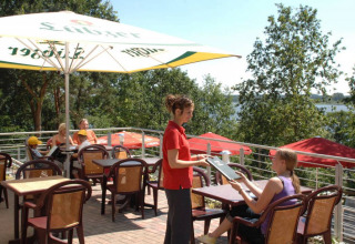 Terrazza esterna al Vakantiepark Havelberge in Meclemburgo-Pomerania con ospiti e cameriera sotto ombrelloni.