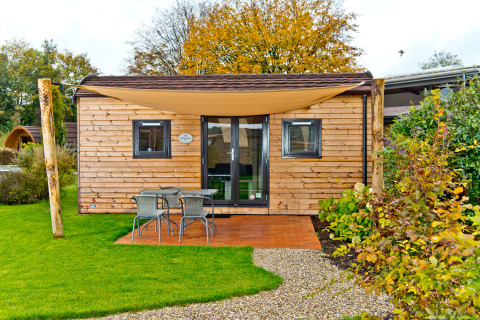 Cabaña de madera con terraza, muebles de jardín y toldo en Campingpark Kerstgenshof, glamping en Alemania.