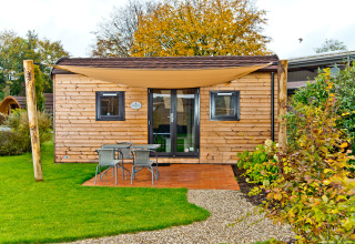 Cabane en bois avec terrasse, mobilier de jardin et voile d'ombrage au Campingpark Kerstgenshof en Allemagne.