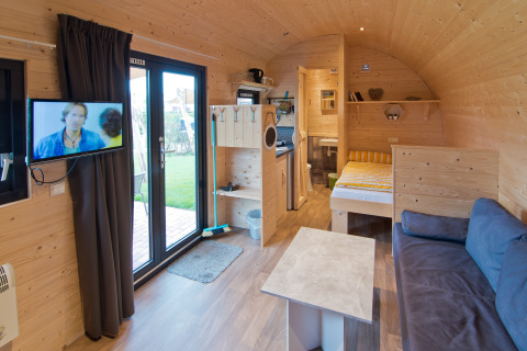 Moderne glamping lodge met bed, bank, tv en kitchenette bij Campingpark Kerstgenshof in Duitsland.