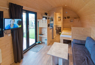 Moderne glamping-indkvartering i træ med dobbeltseng, sofa, tv og stort vindue hos Campingpark Kerstgenshof.