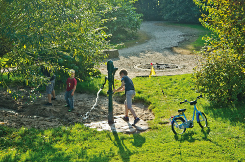 Des enfants jouent à une pompe à eau près de l'herbe et d'un vélo à Campingpark Kerstgenshof - Lodges Allemagne.