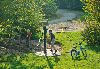 Kids playing at a water pump near grass and a bike at Campingpark Kerstgenshof - Lodges Germany.