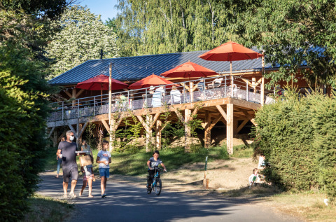 Families walk and cycle near Huttopia Lac de la Siauve glamping with wooden terrace and red parasols in Auvergne.