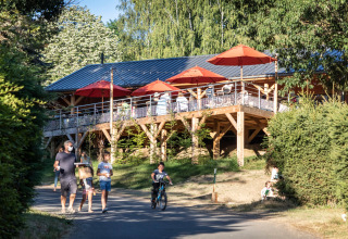Families walk and cycle near Huttopia Lac de la Siauve glamping with wooden terrace and red parasols in Auvergne.