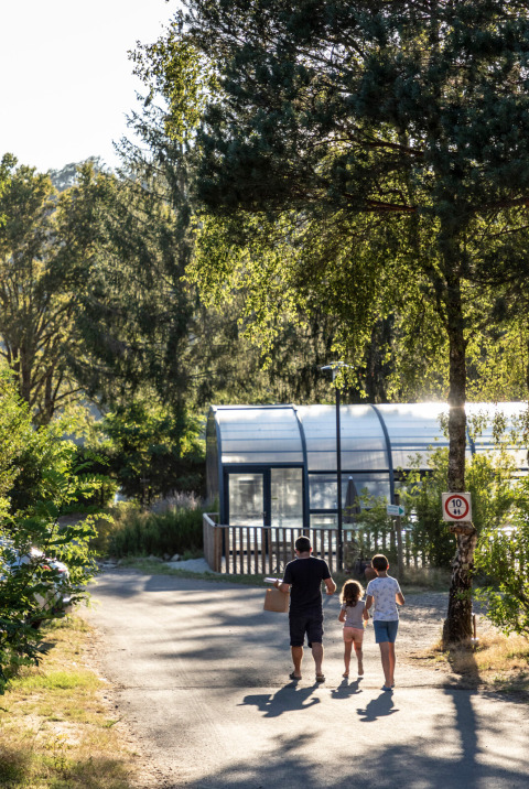 Family walks along a path near greenhouse and trees at Huttopia Lac de la Siauve Glamping Auvergne.